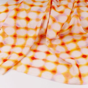 May include: A folded fabric with a repeating pattern of white, orange, and red circles. The fabric has a soft, flowing appearance, with the colors blending together. The background is white.
