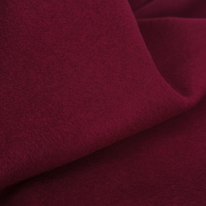 May include: Close-up of a deep burgundy fabric with a soft, textured surface. The material is draped, creating folds and shadows that highlight its plush appearance. The color is a rich, saturated shade of red.