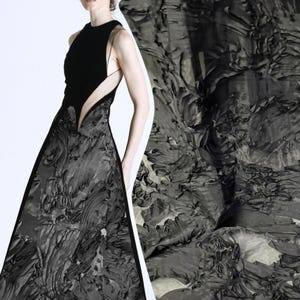 Puede incluir: Un vestido largo sin mangas con un corpiño negro sólido con aberturas laterales y una falda de tela gris oscuro con un patrón texturizado, arremolinado y en capas que se asemeja a pinceladas gruesas o arte en relieve.