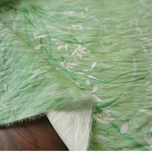 Peut inclure: Tissu vert clair avec un motif floral de fleurs blanches et de tiges vertes. Le tissu pr&eacute;sente une texture l&eacute;g&egrave;rement froiss&eacute;e, avec un motif de style aquarelle. Le tissu est pli&eacute;, r&eacute;v&eacute;lant un envers blanc.