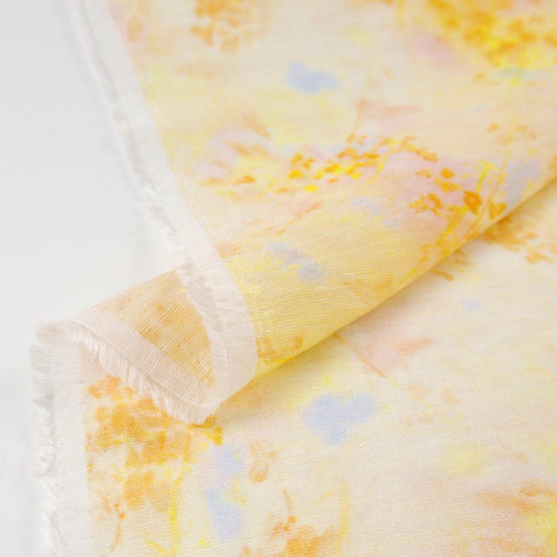 May include: A folded piece of fabric with a watercolor-like pattern. The fabric features a blend of yellow, orange, and light blue hues, creating a soft, artistic design. The edges of the fabric are unfinished, adding a rustic touch. Ideal for crafting or home decor.