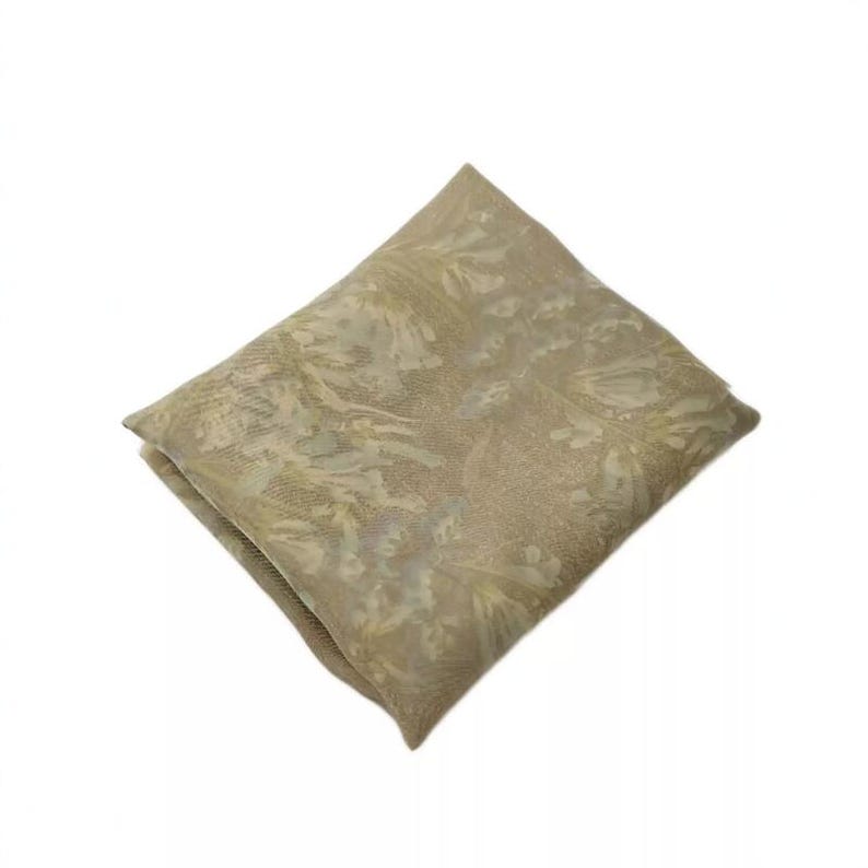 Puede incluir: Una pieza de tela de forma cuadrada en un tono beige apagado, con un sutil patr&oacute;n floral tono sobre tono en todo el material. El tejido est&aacute; doblado en orientaci&oacute;n de diamante, mostrando una textura suave y semitransparente y un tejido delicado.