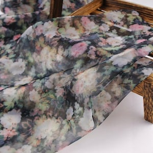 Pu&ograve; includere: Tessuto trasparente con motivo floreale nei toni del rosa, bianco e verde su sfondo scuro. Il tessuto &egrave; drappeggiato su una struttura in legno, evidenziando la sua delicata consistenza e il design. Ideale per sciarpe, abiti o altri capi d'abbigliamento.
