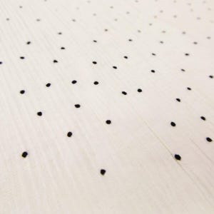 May include: Close-up of a white fabric with a subtle ribbed texture, adorned with evenly spaced black polka dots. The dots are small and create a simple, yet elegant pattern. The fabric appears soft and lightweight.