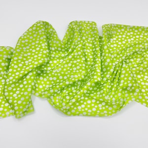 May include: A bright lime green scarf featuring a repeating pattern of white polka dots of varying sizes. The fabric is draped in soft, flowing folds, creating a textured appearance across the surface of the lightweight material.