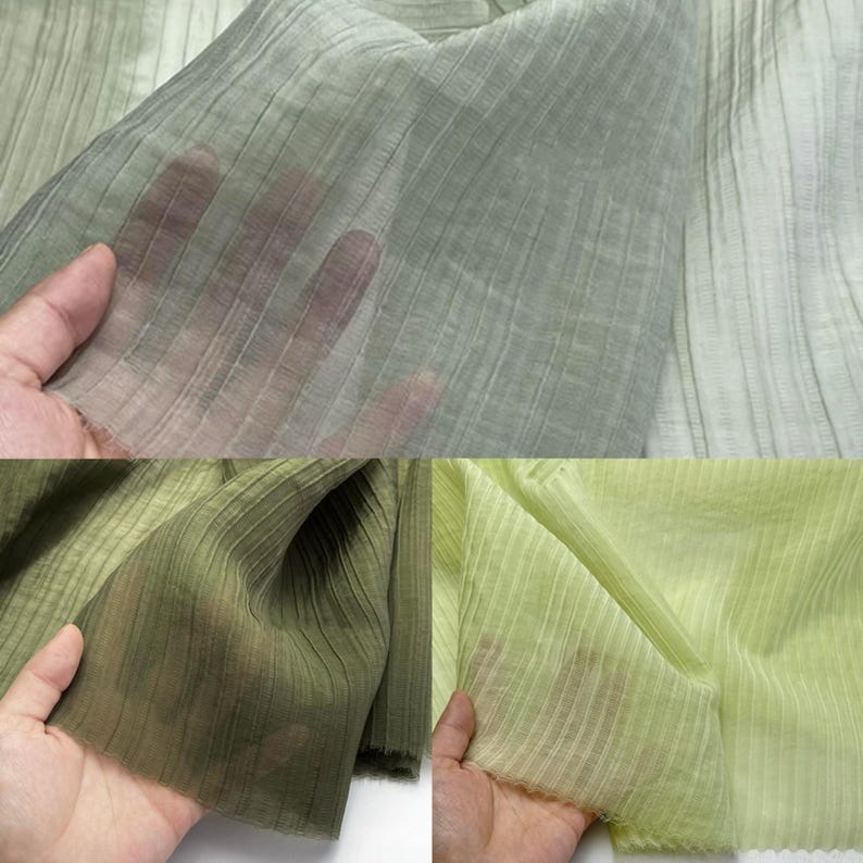 May include: Close-up of sheer, pleated fabric in shades of green. The fabric has a ribbed texture and is semi-transparent, allowing light to pass through. The fabric is held up, showcasing its drape and texture.