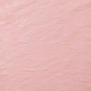 May include: A light pink fabric featuring a subtle, tone-on-tone floral pattern with roses and leaves. The material has a slightly crinkled, textured surface, creating a soft and delicate appearance across the entire visible area of the textile.