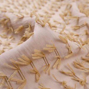 May include: A light beige fabric featuring a textured surface with small, evenly spaced tufted clusters of golden-yellow thread. The material has a soft, woven appearance with a repeating pattern of these raised, fringed decorative elements.