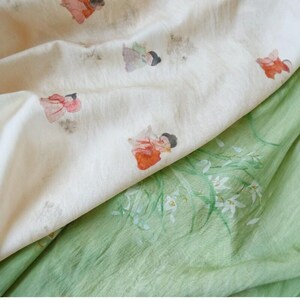 Peut inclure: Gros plan sur deux tissus. L'un est un tissu cr&egrave;me avec des illustrations &agrave; l'aquarelle de personnages en robes rouges et oranges. L'autre est un tissu vert clair avec des motifs floraux blancs.