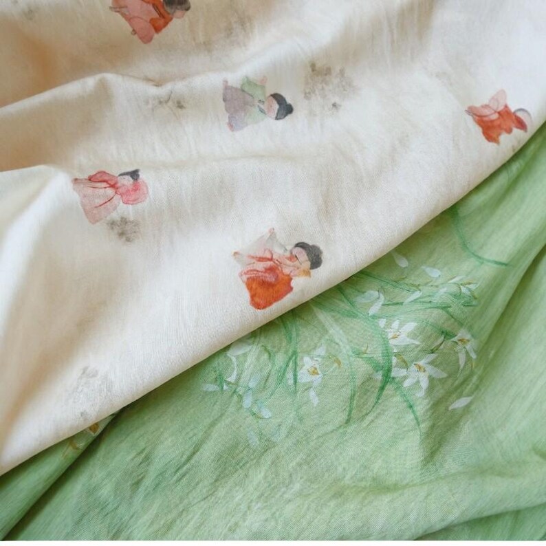 Peut inclure: Gros plan sur deux tissus. L'un est un tissu cr&egrave;me avec des illustrations &agrave; l'aquarelle de personnages en robes rouges et oranges. L'autre est un tissu vert clair avec des motifs floraux blancs.