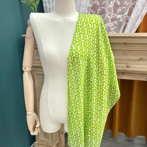 May include: A bright lime green fabric featuring a pattern of white polka dots of varying sizes draped over a cream-colored mannequin torso. The fabric covers the right side of the mannequin, displaying a dense, scattered arrangement of circular spots.