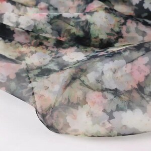 Pu&ograve; includere: Un tessuto trasparente con motivo floreale nei toni del rosa, bianco, verde e grigio. Il tessuto &egrave; drappeggiato, mostrando la sua natura delicata e traslucida. Il motivo floreale &egrave; sparso sulla superficie, creando un morbido effetto acquerello.