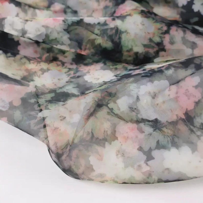 Pu&ograve; includere: Un tessuto trasparente con motivo floreale nei toni del rosa, bianco, verde e grigio. Il tessuto &egrave; drappeggiato, mostrando la sua natura delicata e traslucida. Il motivo floreale &egrave; sparso sulla superficie, creando un morbido effetto acquerello.