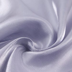 May include: Close-up of a flowing, light purple fabric with a silky sheen. The fabric is draped in soft folds, creating shadows and highlights that emphasize its texture and fluidity. The overall effect is one of elegance and softness.