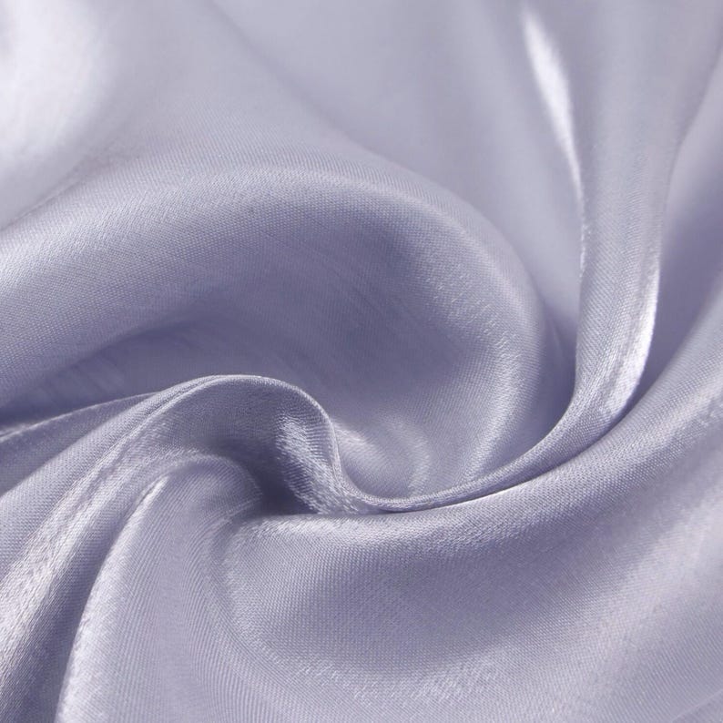 May include: Close-up of a flowing, light purple fabric with a silky sheen. The fabric is draped in soft folds, creating shadows and highlights that emphasize its texture and fluidity. The overall effect is one of elegance and softness.