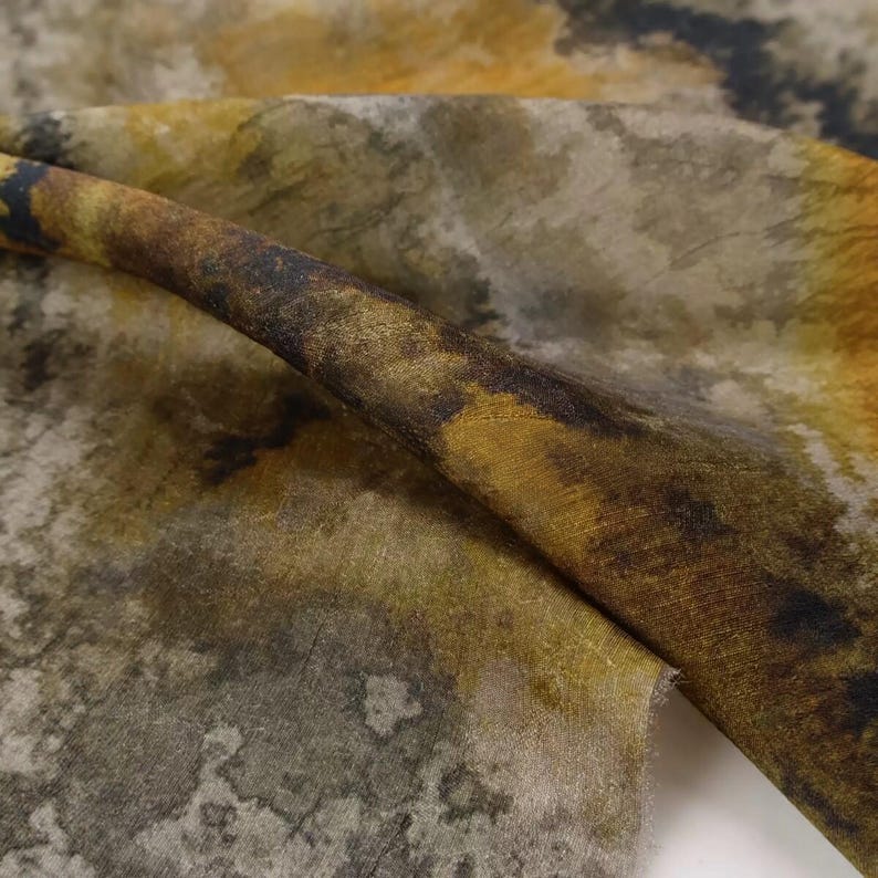 Peut inclure: Un morceau de tissu pr&eacute;sentant un motif abstrait avec des nuances m&eacute;lang&eacute;es de jaune moutarde, de brun fonc&eacute; et de gris sourd. Le textile affiche un aspect textur&eacute; rappelant l'aquarelle avec des transitions de couleurs organiques et tachet&eacute;es.