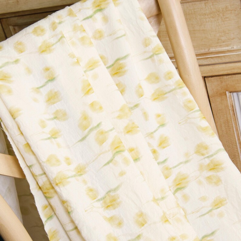 May include: A lightweight fabric featuring a repeating pattern of soft yellow tulips with pale green stems and leaves. The textile has a slightly crinkled texture and a cream-colored background, displaying a delicate floral print throughout the material.