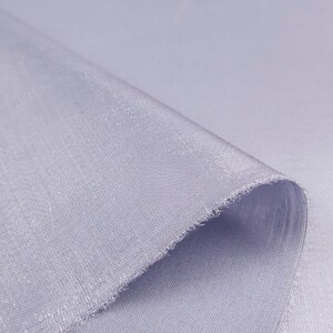 May include: Close-up of a folded piece of light blue fabric. The fabric has a subtle sheen and a slightly textured surface. The edge of the fabric is frayed, revealing the weave.
