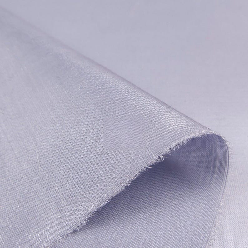 May include: Close-up of a folded piece of light blue fabric. The fabric has a subtle sheen and a slightly textured surface. The edge of the fabric is frayed, revealing the weave.