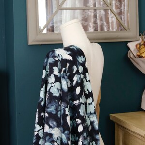 May include: A navy blue fabric draped over a mannequin, featuring a pattern of light blue and white floral shapes. The fabric's design creates a watercolor effect, with soft edges and a flowing appearance. The background includes a mirror and a teal wall.