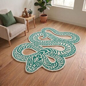 Puede incluir: Una alfombra grande de forma irregular con un diseño de serpiente enroscada. La alfombra es de color crema con un patrón detallado y repetitivo en verde azulado oscuro que perfila el cuerpo, la cabeza y las escamas de la serpiente, creando un efecto visual.