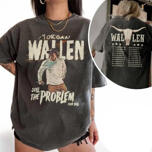 Pode incluir: Camiseta cinza escuro com um gráfico de Morgan Wallen e o texto "MORGAN WALLEN STILL THE PROBLEM TOUR 2026". A parte de trás da camisa exibe um crânio de touro e datas da turnê.