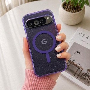 Può includere: Una custodia trasparente per telefono con un design glitterato viola e un bordo viola. La custodia ha un attacco magnetico circolare viola con un logo "G" bianco. La custodia è progettata per un telefono Google Pixel.