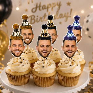 May include: A set of cupcake toppers featuring a person's face with a beard, each wearing a miniature party hat with a pom-pom on top. The hats are labelled with the numbers 20, 30, or 40 in gold or white, set atop frosted cupcakes on a white stand.