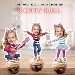 Peut inclure: Trois décorations de cupcake personnalisées avec un motif de poupée chaton. Chaque décoration affiche le visage d'un enfant sur un corps de dessin animé avec des oreilles de chat. Le texte indique PERSONALIZED CUPCAKE TOPEPRS 3 KITTY DOLL.