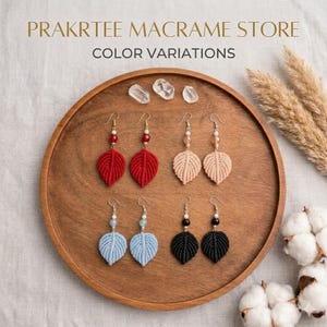 Op de afbeelding: Macramé blad oorbellen in rood, beige, lichtblauw en zwart, gepresenteerd op een houten dienblad. De oorbellen hebben goudkleurige haken en kralenaccenten. De tekst "PRAKRTEE MACRAME STORE COLOR VARIATIONS" is zichtbaar.