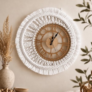 May include: A round wall clock featuring a light brown wooden frame with Roman numerals and black hands, surrounded by a thick, white macrame border with intricate knotted patterns and a long, fringed edge that extends around the entire circumference.