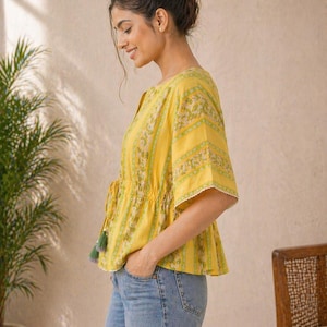 Puede incluir: Top amarillo con estampado floral y mangas cortas. El top tiene un cord&oacute;n en la cintura y ribete de encaje blanco. Las mangas son cortas y acampanadas. El top se combina con unos vaqueros azules.