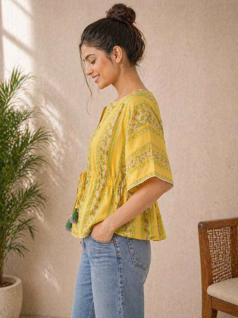 Puede incluir: Top amarillo con estampado floral y mangas cortas. El top tiene un cord&oacute;n en la cintura y ribete de encaje blanco. Las mangas son cortas y acampanadas. El top se combina con unos vaqueros azules.