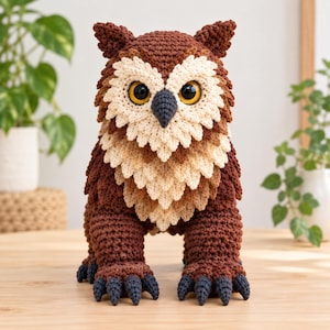 May include: A crocheted owl figurine featuring a dark brown body with textured plumage, a cream-colored chest and facial disc, large yellow eyes with black pupils, and a dark gray beak. The creature has four feet with dark gray claws.