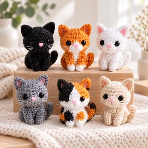May include: Six small crocheted cat figurines arranged on a wooden block. The cats feature black, orange, white, gray, calico, and beige yarn colors. Each cat has large black plastic eyes, a small pink stitched nose, and white thread whiskers.