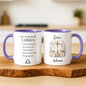 Könnte beinhalten: Zwei weiße Keramiktassen mit violetten Henkeln und Innenseiten. Eine Tasse zeigt den Text THE POWER OF LIBRA mit Aufzählungspunkten zu Eigenschaften und dem Waage-Symbol. Die andere Tasse zeigt das Wort Libra, den Namen Julienne und eine Waage.