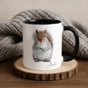 Puede incluir: Taza de cerámica blanca con interior y asa negros. La taza presenta una ilustración detallada de una ardilla con pelaje gris y marrón. El nombre "Amelie" está escrito en cursiva en la taza.