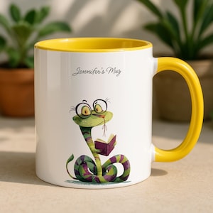 May include: White ceramic mug with a yellow interior and handle. The mug features a cartoon snake wearing glasses and reading a book. The text "Jennifer's Mug" is printed on the mug.