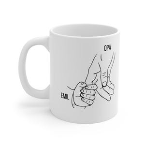 Könnte beinhalten: Weiße Keramik-Tasse mit einer schwarzen Strichzeichnung von zwei Händen, die sich an den Händen halten. Das Wort "OPA" steht über der größeren Hand, und der Name "EMIL" steht neben der kleineren Hand.