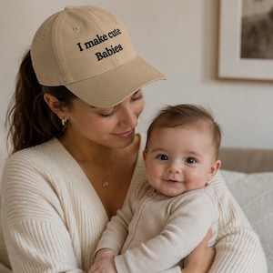 Può includere: Un cappellino da baseball beige con il testo ricamato in nero "I make cute Babies" sul pannello frontale. Il cappellino presenta una corona strutturata, una visiera curva e un bottone sulla parte superiore, con una classica struttura a sei pannelli.