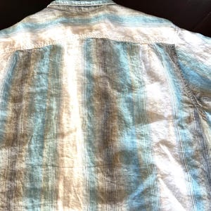 May include: A light blue, white, and brown striped button-down shirt. The shirt has short sleeves and a classic collar. The fabric appears to be lightweight and suitable for warm weather.