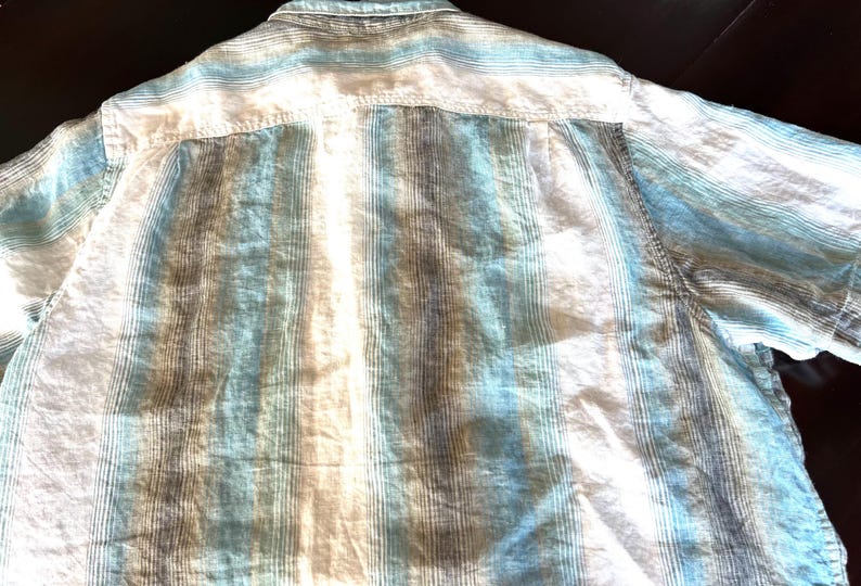 May include: A light blue, white, and brown striped button-down shirt. The shirt has short sleeves and a classic collar. The fabric appears to be lightweight and suitable for warm weather.
