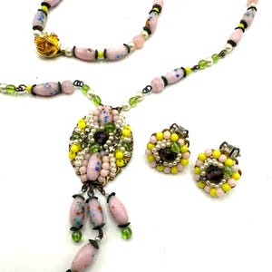May include: A vintage jewelry set featuring a necklace and matching earrings. The necklace has pink, white, and green beads, with a pendant of pink and yellow beads. The earrings are round with yellow and pink beads.