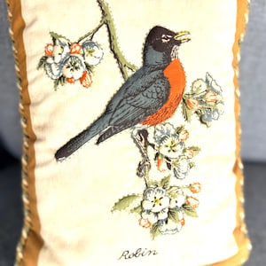 May include: A rectangular throw pillow with a cream-colored center panel featuring a printed illustration of a robin perched on a flowering branch. The bird has a dark head, gray wings, and an orange breast. The word Robin is printed below.