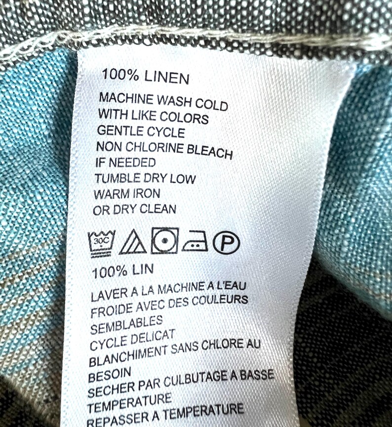 May include: A white fabric label with black text providing care instructions for a linen item. The label states "100% LINEN" and includes washing, drying, and ironing instructions, along with care symbols.