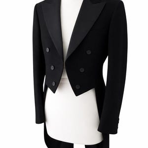 Könnte beinhalten: Eine formelle schwarze Smokingjacke mit fallendem Revers und doppelreihigem Verschluss. Die Jacke hat ein Frackdesign und wird auf einer weißen Schaufensterpuppe präsentiert. Die Ärmel sind lang und die Jacke hat einen klassischen, eleganten Stil.