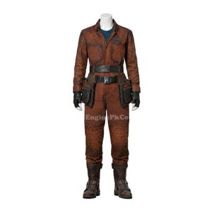 May include: A brown jumpsuit with a matching belt, tool pockets, and boots. The outfit has a textured appearance and is worn with black gloves. The jumpsuit has a blue undershirt and a small patch on the chest. The text "EnginePkCo" is visible.