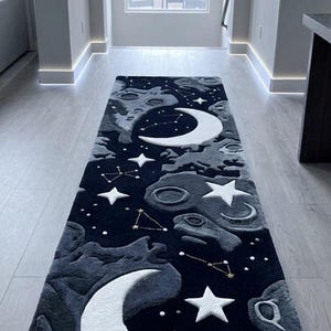 Op de afbeelding: Een lang, rechthoekig tapijt met een hemels ontwerp. Het tapijt heeft een donkerblauwe achtergrond met witte halve manen, sterren en sterrenbeelden. Het tapijt is ongeveer 244 cm lang.