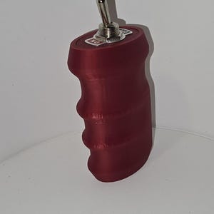 May include: A dark red, ergonomically shaped handle with a metallic toggle switch mounted on the top surface. The switch base features a small white label with the text ON printed in red, indicating the operational position of the toggle mechanism.