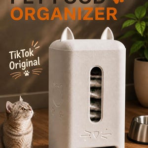 Puede incluir: Un organizador de comida para mascotas de color crema, rectangular, con detalles en forma de orejas de gato en la parte superior, una ventana vertical y una ranura de dispensación. Incluye el texto PET FOOD ORGANIZER y TikTok Original.